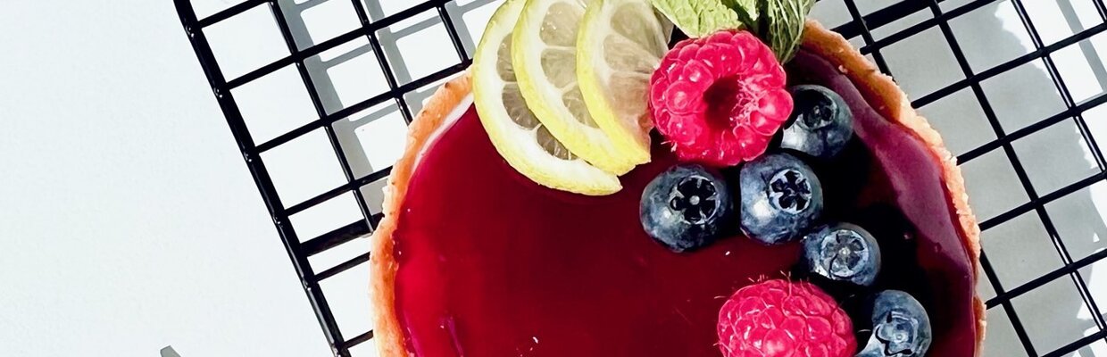 Ein kleiner Kuchen mit roter Glasur, garniert mit Beeren und Zitronenscheiben, auf einem Gitterrost.